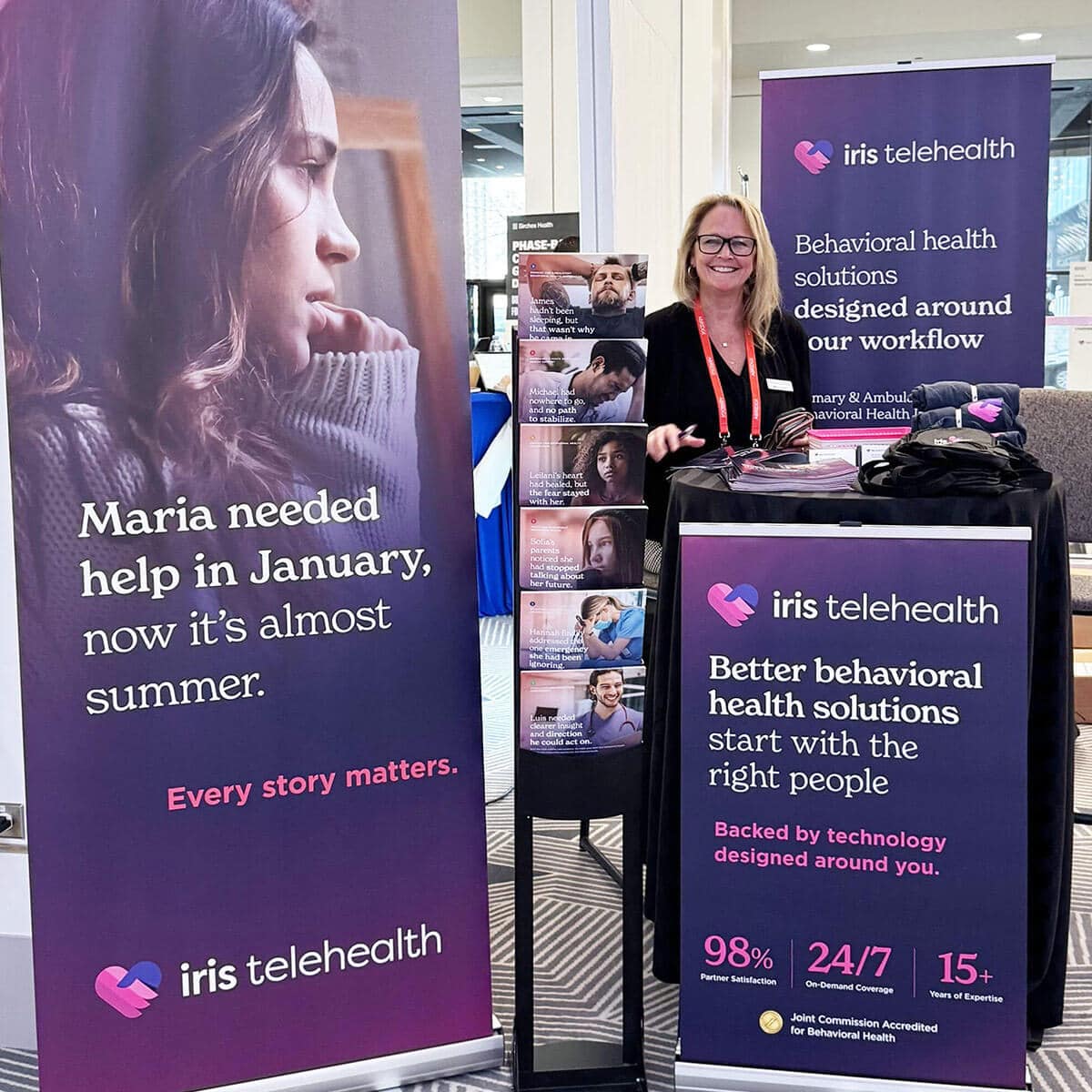 Booth for iris telehealth with banners showing stories of people and a smiling staff member at a table of brochures.